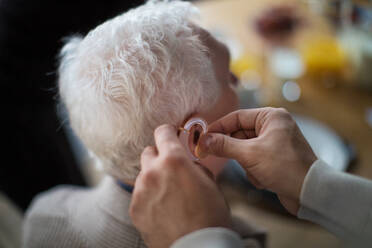 A close-up of caregiver man's hand inserting hearing aid in senior's man ear. - HPIF03623