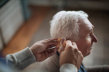 A close-up of caregiver man's hand inserting hearing aid in senior's man ear. - HPIF03624