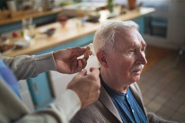 A caregiver helping senior man to insert hearing aid in his ear. - HPIF03625