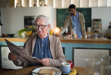 Ein älterer Mann genießt sein Frühstück und liest Zeitung in einem Pflegeheim. - HPIF03628