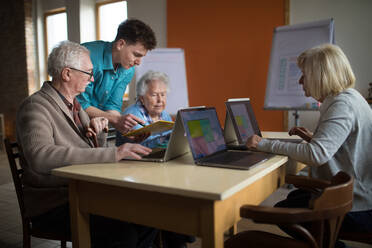 Eine Seniorengruppe in einem Altersheim mit einem jungen Lehrer, der gemeinsam in einem Computerkurs lernt - HPIF03639
