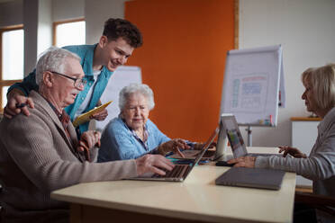 Eine Seniorengruppe in einem Altersheim mit einem jungen Lehrer, der gemeinsam in einem Computerkurs lernt - HPIF03641