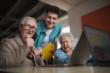 Eine Seniorengruppe in einem Altersheim mit einem jungen Lehrer, der gemeinsam in einem Computerkurs lernt - HPIF03642