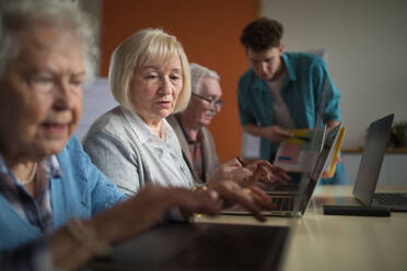 Eine Seniorengruppe in einem Altersheim mit einem jungen Lehrer, der gemeinsam in einem Computerkurs lernt - HPIF03644