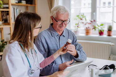 A healthcare worker or caregiver visiting senior man indoors at home, explaining medicine dosage. - HPIF03650