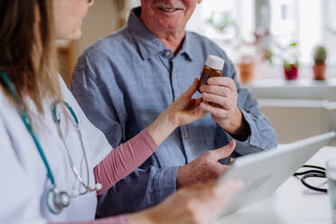 Eine medizinische Fachkraft oder eine Pflegekraft besucht einen älteren Mann zu Hause und erklärt ihm die Medikamentendosierung. - HPIF03651