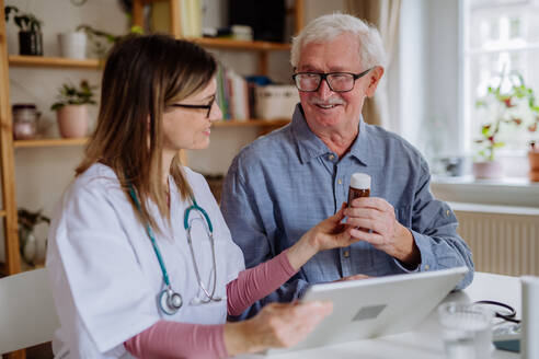 A healthcare worker or caregiver visiting senior man indoors at home, explaining medicine dosage. - HPIF03652