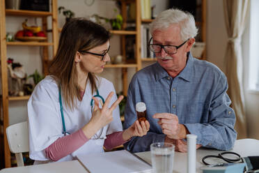 A healthcare worker or caregiver visiting senior man indoors at home, explaining medicine dosage. - HPIF03654