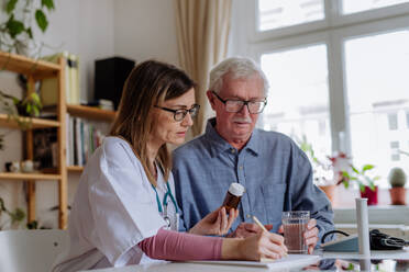 Eine medizinische Fachkraft oder eine Pflegekraft besucht einen älteren Mann zu Hause und erklärt ihm die Medikamentendosierung. - HPIF03657