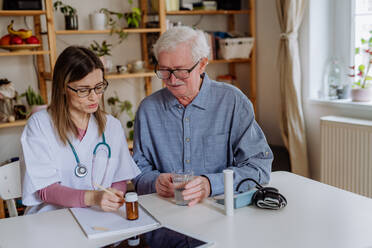 Eine medizinische Fachkraft oder eine Pflegekraft besucht einen älteren Mann zu Hause und erklärt ihm die Medikamentendosierung. - HPIF03658