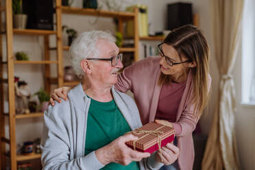 Eine glückliche Frau überrascht ihren älteren Vater, als sie ihn zu Hause besucht und ein Geschenk mitbringt. - HPIF03671