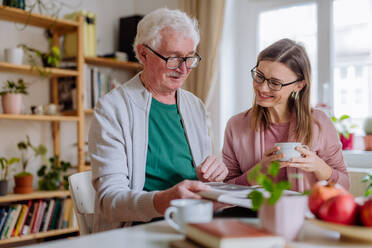 Eine erwachsene Tochter besucht ihren älteren Vater zu Hause und trinkt gemeinsam Kaffee, während sie sich ein Buch ansieht. - HPIF03676