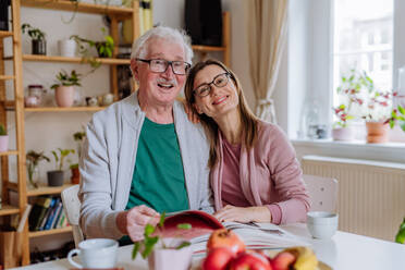 Eine erwachsene Tochter besucht ihren älteren Vater zu Hause und trinkt gemeinsam Kaffee, während sie sich ein Buch ansieht. - HPIF03677