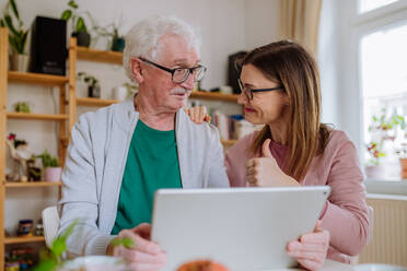 An adult daughter visiting her senior father at home and using tablet. - HPIF03679