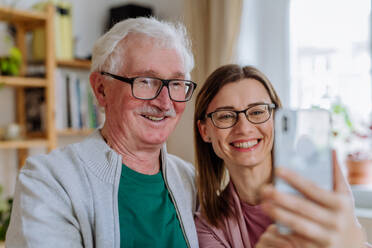 Eine erwachsene Tochter besucht ihren älteren Vater zu Hause und macht ein Selfie. - HPIF03680