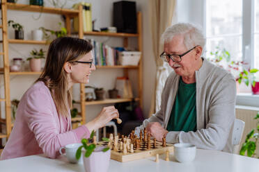 Eine erwachsene Tochter besucht ihren älteren Vater zu Hause und spielt mit ihm Schach. - HPIF03682