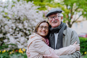 Eine erwachsene Tochter umarmt ihren älteren Vater draußen im Park an einem Frühlingstag. - HPIF03688