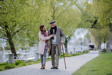 A happy senior man with walking stick and adult daughter outdoors on a walk in park. - HPIF03691