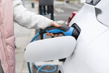 Woman plugging charger in car at station - EKGF00197