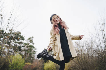 Smiling girl with pink hair standing in park under sky - MDOF00401