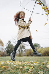 Cheerful girl jumping with umbrella in park - MDOF00407