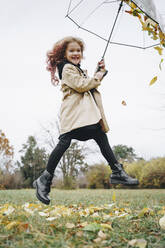 Fröhliches Mädchen springt mit Regenschirm im Park - MDOF00407