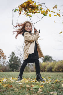 Cheerful girl having fun with umbrella in park - MDOF00408