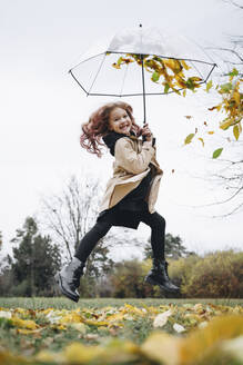 Cheerful cute girl jumping with umbrella in park - MDOF00409