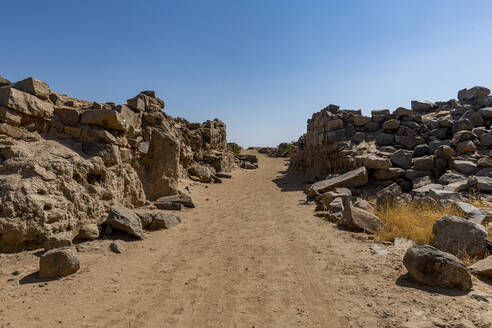 Leere unbefestigte Straße inmitten von Felsen unter blauem Himmel in der archäologischen Stätte Al-Ukhdud in Najran, Saudi-Arabien - RUNF04735