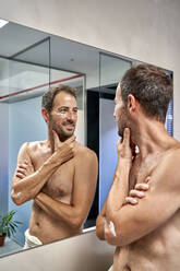 Smiling man with hand on chin looking in mirror - VEGF06102