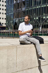 Mann mit Smartphone sitzt vor einem Gebäude - VEGF06117
