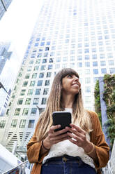 Happy woman with mobile phone in front of building - VEGF06132