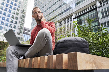 Man sitting with laptop in front of modern buildings - VEGF06135