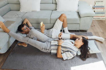 Girl and boy using smart phone lying on carpet in living room at home - EGHF00690