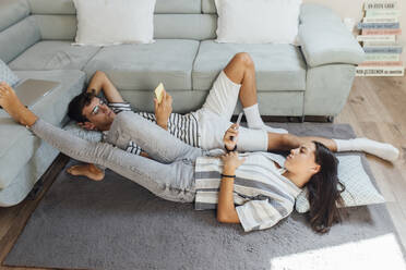 Mädchen und Junge mit Smartphone auf Teppich im Wohnzimmer liegend zu Hause - EGHF00690