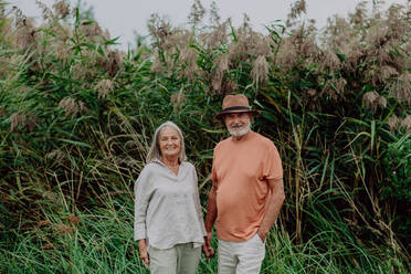Glückliches älteres Paar bei einem Spaziergang in der Nähe des Sees an einem bewölkten Herbsttag. - HPIF03731