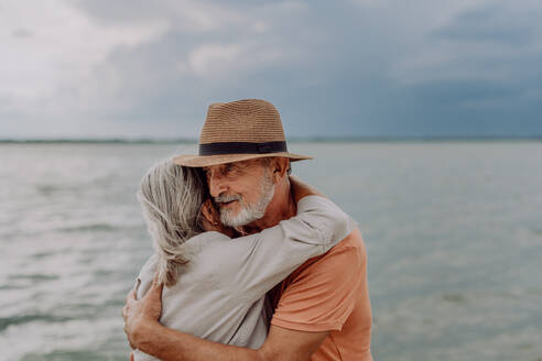 Verliebtes älteres Paar, das sich umarmt und einen romantischen Moment am herbstlichen Meer verbringt. - HPIF03745