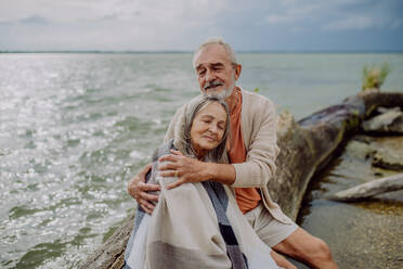 Ein älteres Paar sitzt und hat einen romantischen Moment am herbstlichen Meer. - HPIF03751
