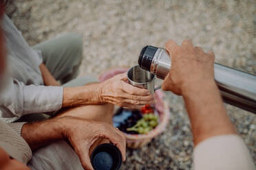 Nahaufnahme eines älteren Paares beim Picknick am Strand an einem Herbsttag, das Tee aus einer Thermoskanne trinkt. - HPIF03754