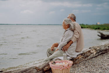 Älteres Paar sitzt mit Picknickkorb, entspannt und hat einen romantischen Moment am herbstlichen Meer. - HPIF03755