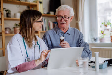Eine medizinische Fachkraft oder eine Pflegekraft besucht einen älteren Mann zu Hause und erklärt ihm die Medikamentendosierung. - HPIF03761