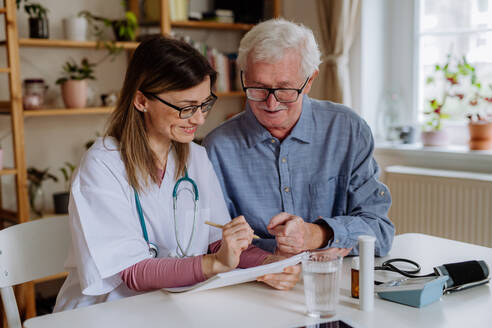 A healthcare worker or caregiver visiting senior man indoors at home, explaining medicine dosage. - HPIF03762
