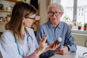 A healthcare worker or caregiver visiting senior man indoors at home, explaining medicine dosage. - HPIF03763