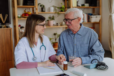 A healthcare worker or caregiver visiting senior man indoors at home, explaining medicine dosage. - HPIF03765