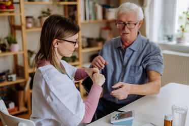 Eine Ärztin besucht einen älteren Mann, untersucht ihn zu Hause und misst den Blutdruck. - HPIF03771