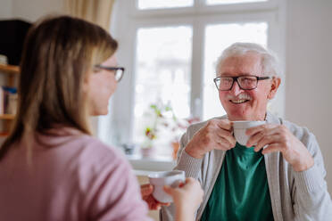 Eine erwachsene Tochter, die ihren älteren Vater zu Hause besucht und mit ihm Kaffee trinkt und sich unterhält. - HPIF03787