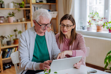 An adult daughter visiting her senior father at home and using tablet. - HPIF03794