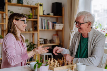 Eine erwachsene Tochter besucht ihren älteren Vater zu Hause und spielt mit ihm Schach. - HPIF03796
