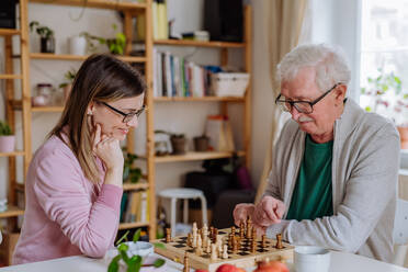 Eine erwachsene Tochter besucht ihren älteren Vater zu Hause und spielt mit ihm Schach. - HPIF03797