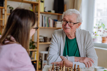 Eine erwachsene Tochter besucht ihren älteren Vater zu Hause und spielt mit ihm Schach. - HPIF03798